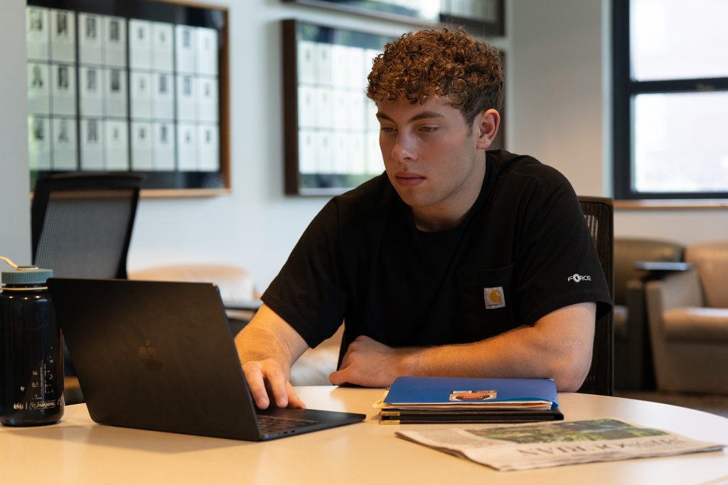 Theo Agniel sitting at a small table and scrolling on his laptop.