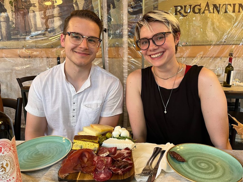 Morgan Davi and Xander Negozio pose for a picture in front of food in Italy.