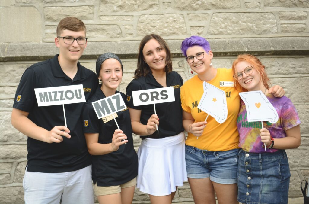Five Honors College students smiling and holding "Mizzou", "MIZ", and "-ORS" signs